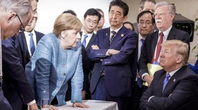The image depicts the German Chancellor in an assertive pose, planting both hands firmly on a table as she addresses the US President - Sakshi Post