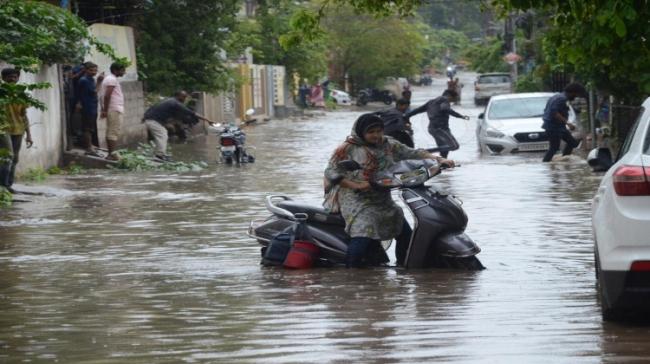 A woman trying to move her scooty in a waterlogged street A woman trying to move her scooty in a waterlogged street - Sakshi Post